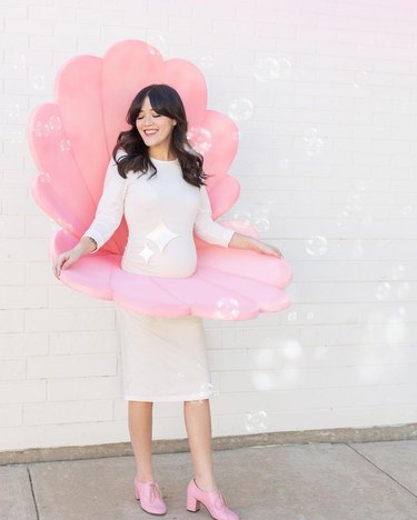 Pregnant woman in white dress wearing a pink oyster costume