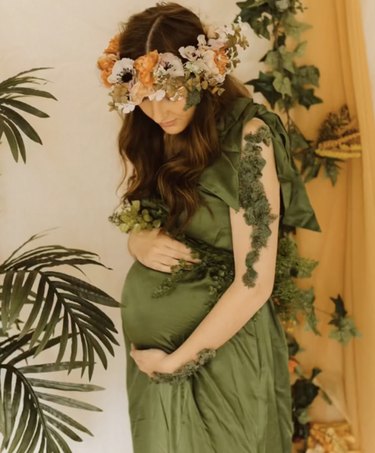 Pregnant woman wearing green dress and a flower crown with fake moss on her arms