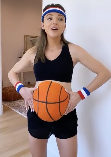 Pregnant woman wearing black shorts and top with her belly painted orange to resemble a basketball