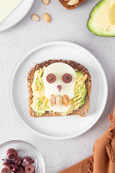 Skull Halloween avocado toast with cheese, olives and pumpkin seeds