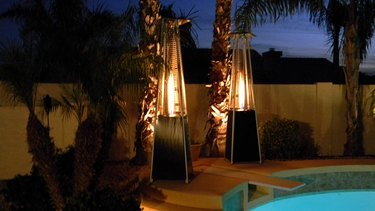 Two Hiland "Pyramid" patio heaters, pictured in the dark on a pool deck, with flame visible in their glass tube interiors