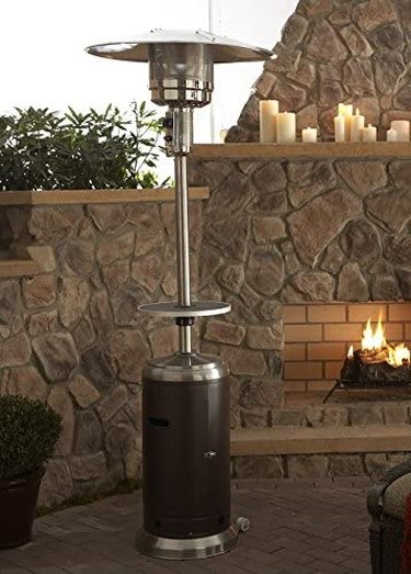 AZ Hiland propane patio heater, pictured on a patio in front of a large outdoor stone fireplace