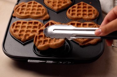 Removing waffles from waffle iron using metal tongs.