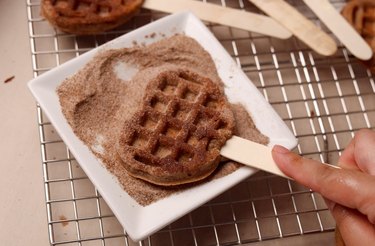 Coating mochi waffle in cinnamon sugar.