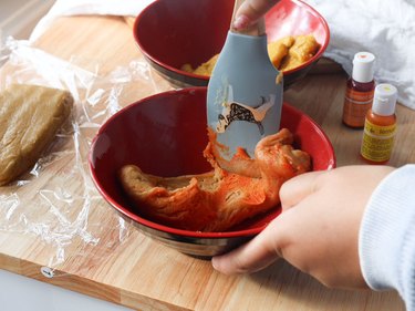 Coloring cookie dough with orange and yellow food coloring.