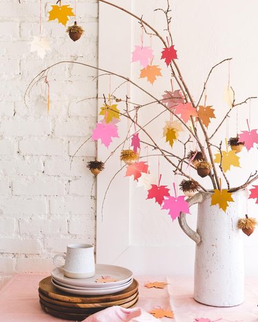 Branches in a white pitcher with hanging paper leaves