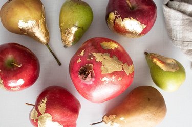 Various fruit with edible gold leaf laid out on a white surface