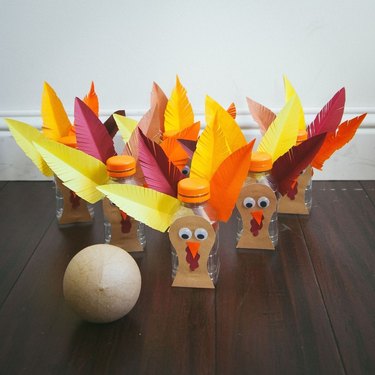 Water bottles decorated to look like turkeys arranged as bowling pins next to a tan sphere