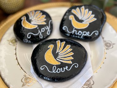 Painted turkey gratitude rocks on a gold-and-white plate with linen napkin