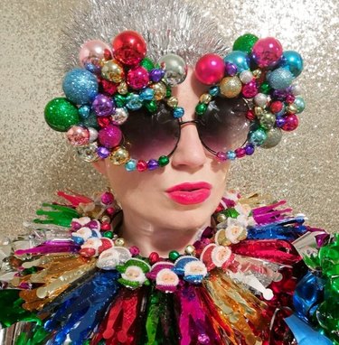 Woman wearing eyewear and collar decorated with metallic baubles and sparkly Santa Claus figurines in jewel tones