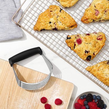 A broad pastry blender with a large, soft, rubberized black handle placed near sheet of freshly-baked scones.