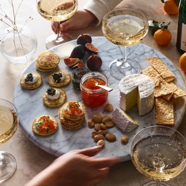 Marble lazy Susan, shown on a tabletop with crackers, cheese, condiments, fresh fruit and glasses of sparkling wine