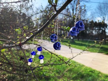 Three pairs of blue earrings hanging from a tree: two sets of blue skulls, one set of small blue mushrooms