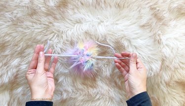 A person threading yarn through a fur pom pom