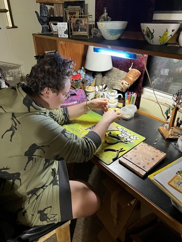 Nicole Hayden sits at a crafting table, working on a pair of small brown mushroom earrings