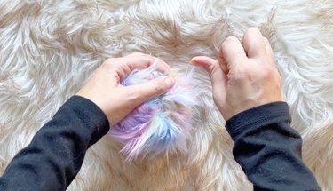 A person stiching a fur pom pom closed.