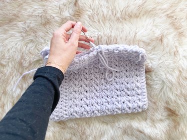 A crochet rectangle folded in half and a person stitching up the sides.