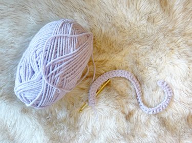 A lavender yarn skein with a row of double crochet stitches and a gold crochet hook.