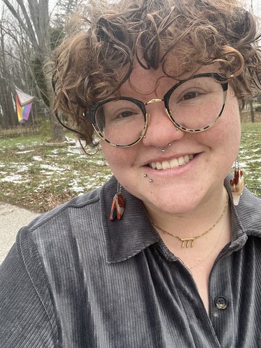 Nicole Hayden smiles, wearing large glasses and a pair of natural stone fidget earrings.