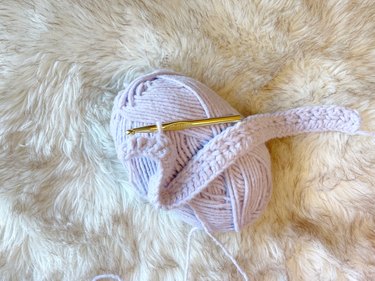 A lavender yarn skein with two rows of crochet stitches and a gold crochet hook.
