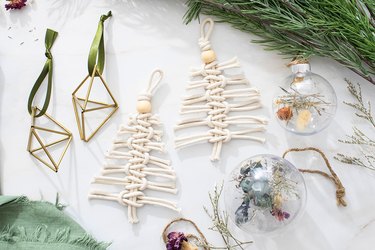 Handmade ornaments made of rope, glass, dried flowers and ribbon set out next to pine branches.