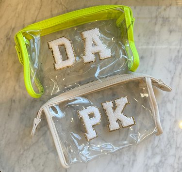 Two clear makeup bags, one with neon green piping and the initials DA in white puffy letters; and the other with ivory piping and the initials PK in white puffy letters