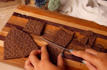 Cutting chocolate graham cracker in half with serrated knife on a cutting board