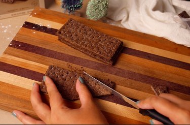 Cutting chocolate graham cracker with serrated knife on a cutting board