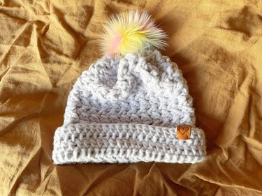 A lavender crochet beanie with a rainbow pom pom.