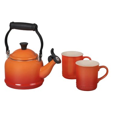 Le Creuset kettle and two matching mugs in an ombre orange hue.