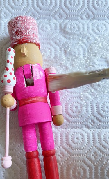 A pink and red nutcracker being painted with paste.