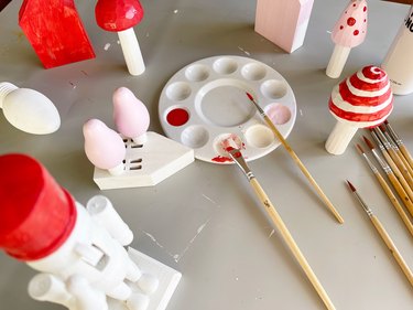 Wooden mushrooms, a nutcracker and houses being painted in red, pink and white paint.