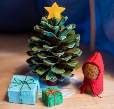 Small felt figure and gift boxes next to pine cone tree