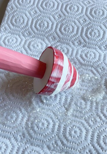 A pink, red, and white mushroom being rolled in clear glitter.