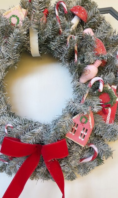 A flocked Christmas tree wreath decorated with colorful wooden figurines in red, pink, and white.