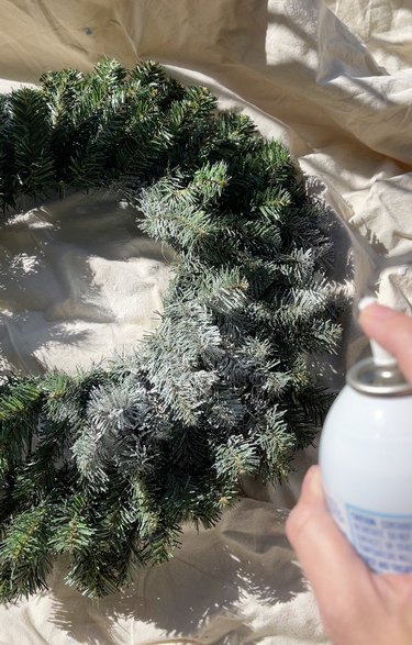 A green Christmas tree wreath being sprayed with fake snow.