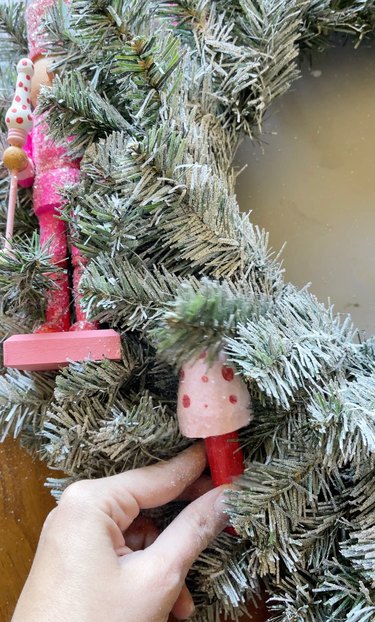 A flocked Christmas tree wreath with a person adding a pink and red mushroom figurine to it.