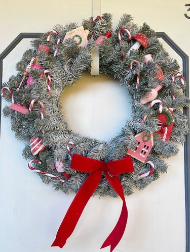 A flocked Christmas tree wreath with holiday houses, mushrooms, and candy canes, topped with a bow.