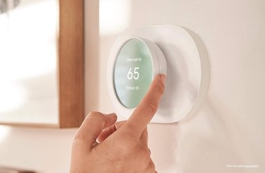 Person's hand adjusting temperature on wall-mounted Google Nest thermostat.
