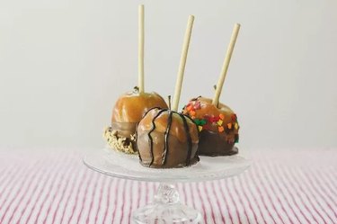 Three caramel apples with chocolate and candies on a cake stand