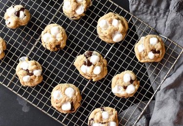Cookies with chocolate pieces and mini marshmallows sit on a cooling rack