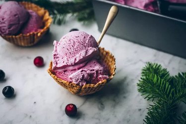 A bowl of pink ice cream surrounded by cranberries