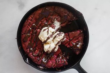 A red velvet cookie in a cast iron skillet, topped with ice cream and metled chocolate