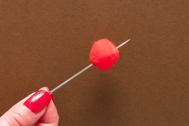 Threading red pompom on needle and thread