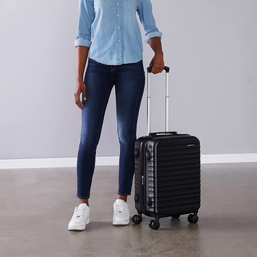 Modern woman standing next to Amazon Basics 21-Inch Hardside Spinner Luggage (Black)