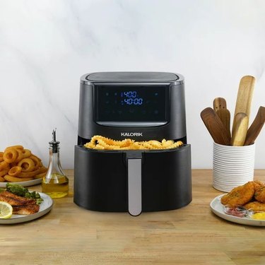 Kalorik 8-quart air fryer cooking 2 pounds of French fries on a wooden countertop.