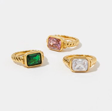 Three gold rings with center stones: pink, emerald green and clear white