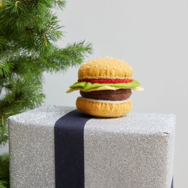 A felt ornament shaped like a burger with lettuce, tomatoes and cheese.
