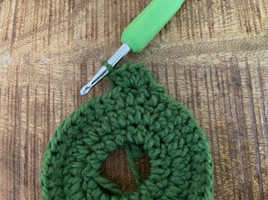 A closeup of a green crochet wreath applique and the start of a scallop-shaped border