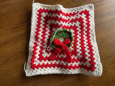 A green crochet wreath with a red bow on top of a giant red and white granny square